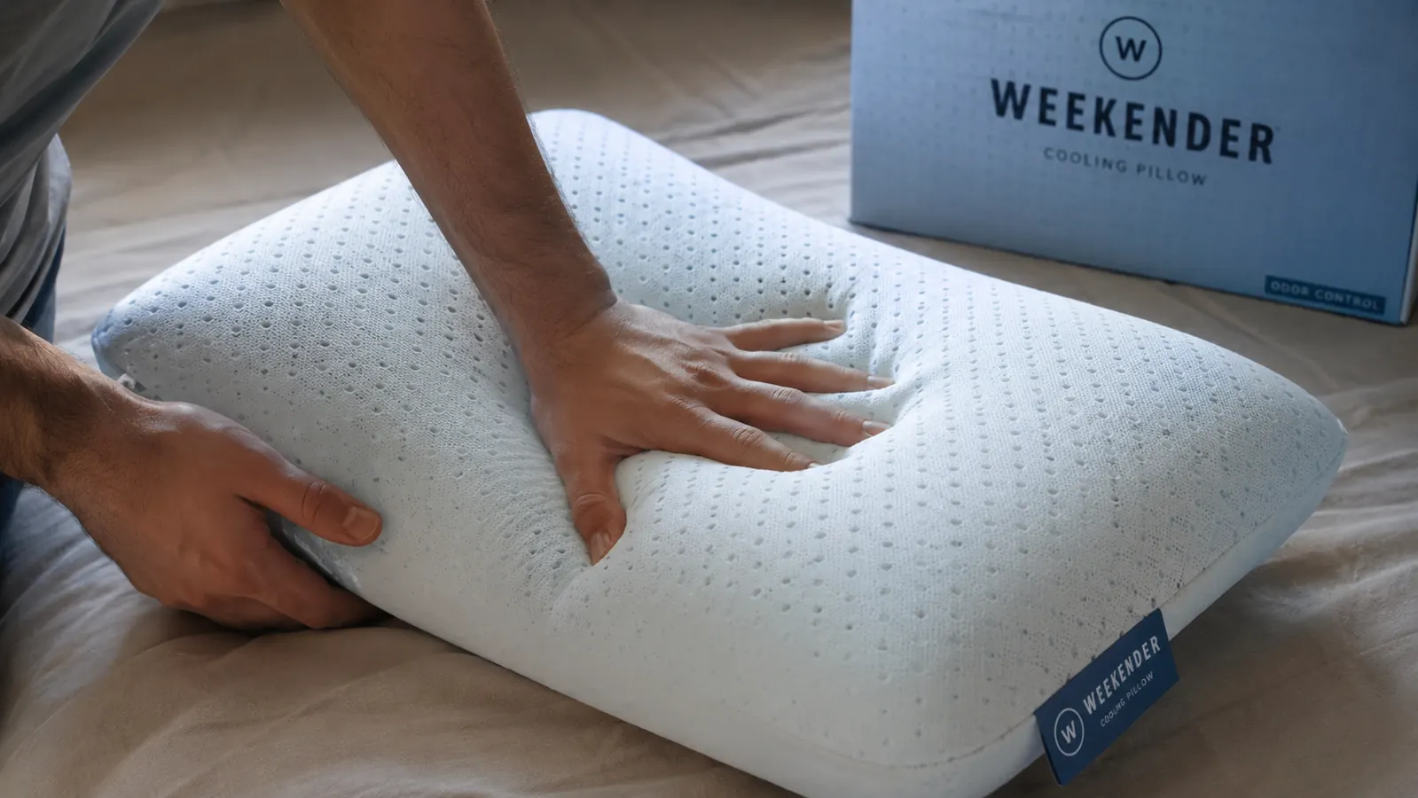 A hand pressing into the Weekender cooling gel memory foam pillow to show the ventilated open-cell texture