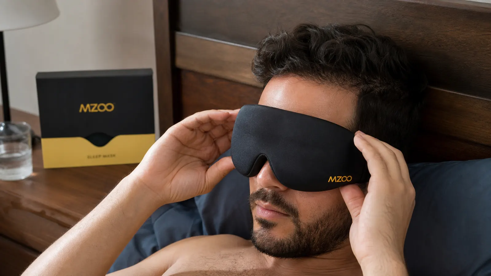 A hand adjusting the contoured eye cups of a black sleep mask before pulling the strap over the head