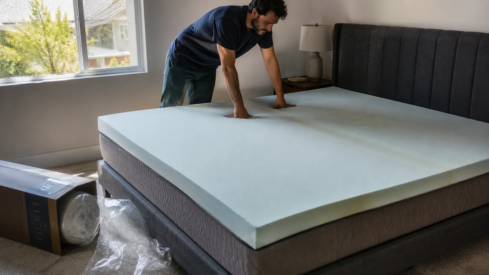 A rolled mattress topper box freshly opened on a bare full-size mattress with a faint fold crease visible across the foam
